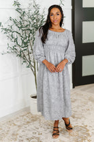 Woman wearing a gray dress standing indoors with a plant in the background