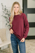 Model wearing a dark burgundy drop shoulder pullover with ribbed cuffs and neckline.