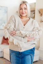 A woman wearing a beige cardigan with looped fringe on the sleeves and button front.