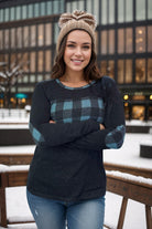 Woman wearing a teal plaid pullover with elbow patches, standing outdoors in the snow.