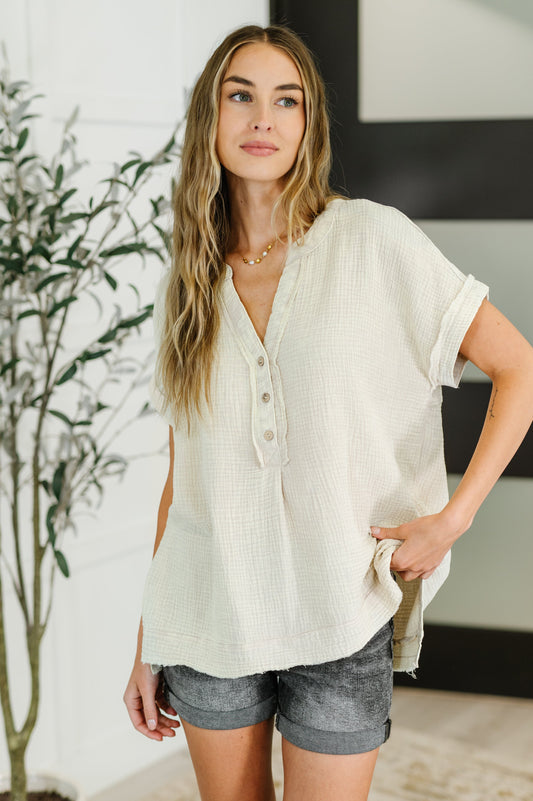 Woman wearing a light-colored blouse and gray shorts indoors with a plant in the background