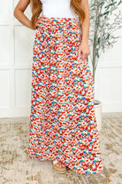 A woman wearing a high-waisted, pleated, floral maxi skirt with a smocked elastic back waist and a thigh-high side slit.