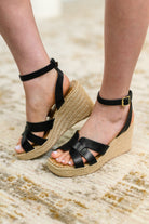 Black wedge sandals with jute sole worn on a textured surface