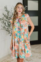 Woman wearing a colorful patterned dress indoors with a plant in the background