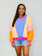A woman wearing a color block pullover with dolman sleeves and ribbed cuffs, in shades of blue, pink, orange, and purple.