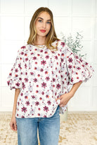 A woman wearing a white balloon sleeve blouse with a floral pattern, paired with blue jeans.