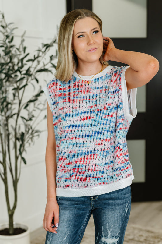 Woman wearing a sleeveless, multicolored patterned top with a blurred indoor background
