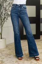 Blue flared jeans worn by a Woman indoors with a plant and decorative wall in the background.
