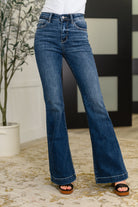 A pair of dark wash high-rise trouser flare jeans with a zip fly, modeled on a neutral background.