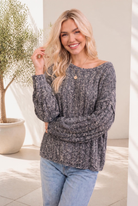 A woman wearing a heathered purple cable knit sweater with balloon sleeves and a relaxed boat neckline.