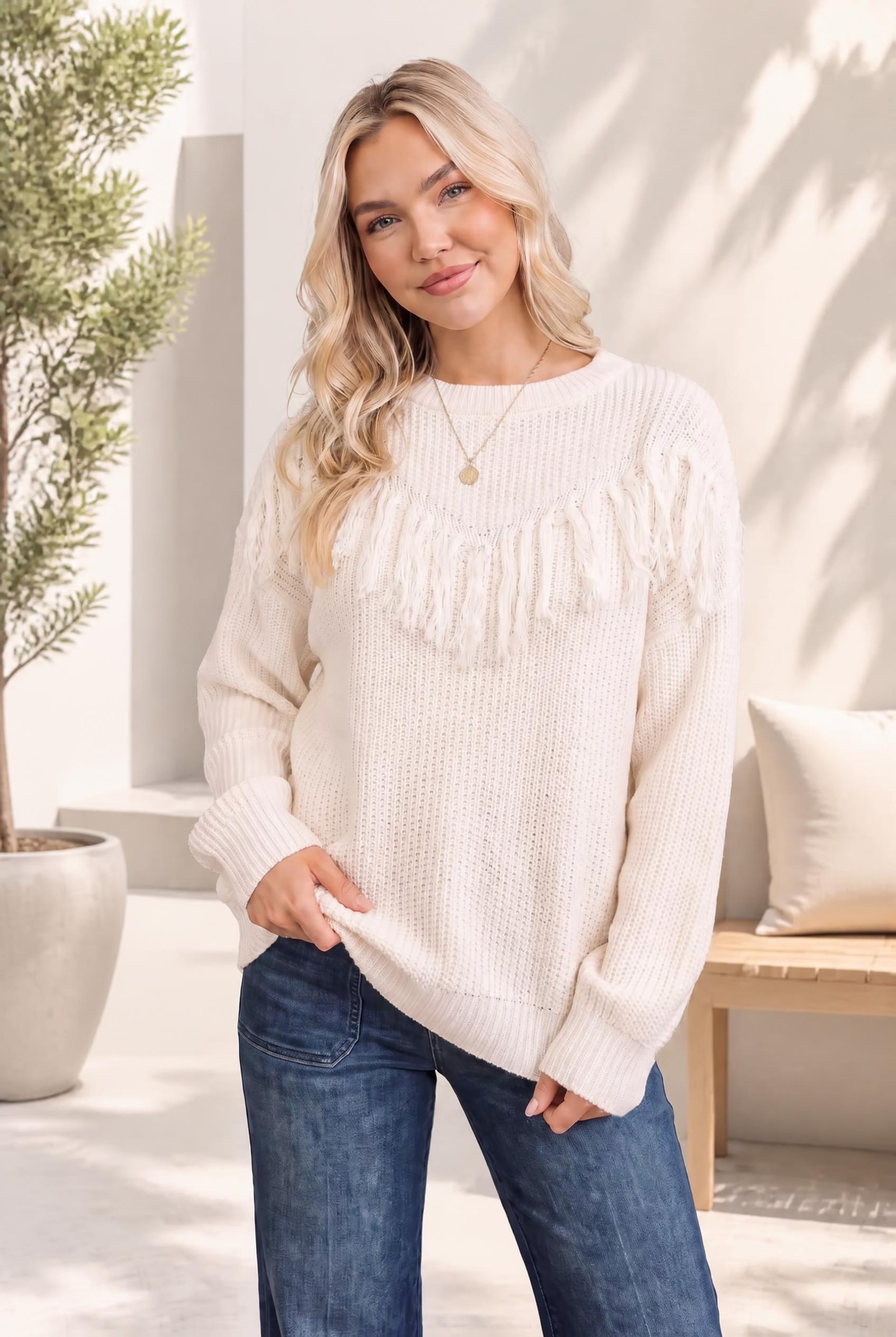 Cream knit sweater with fringe detail, chunky waffle texture, and crew neckline worn by a model with jeans.