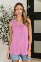 Woman wearing a pink sleeveless top with buttons and denim shorts indoors.