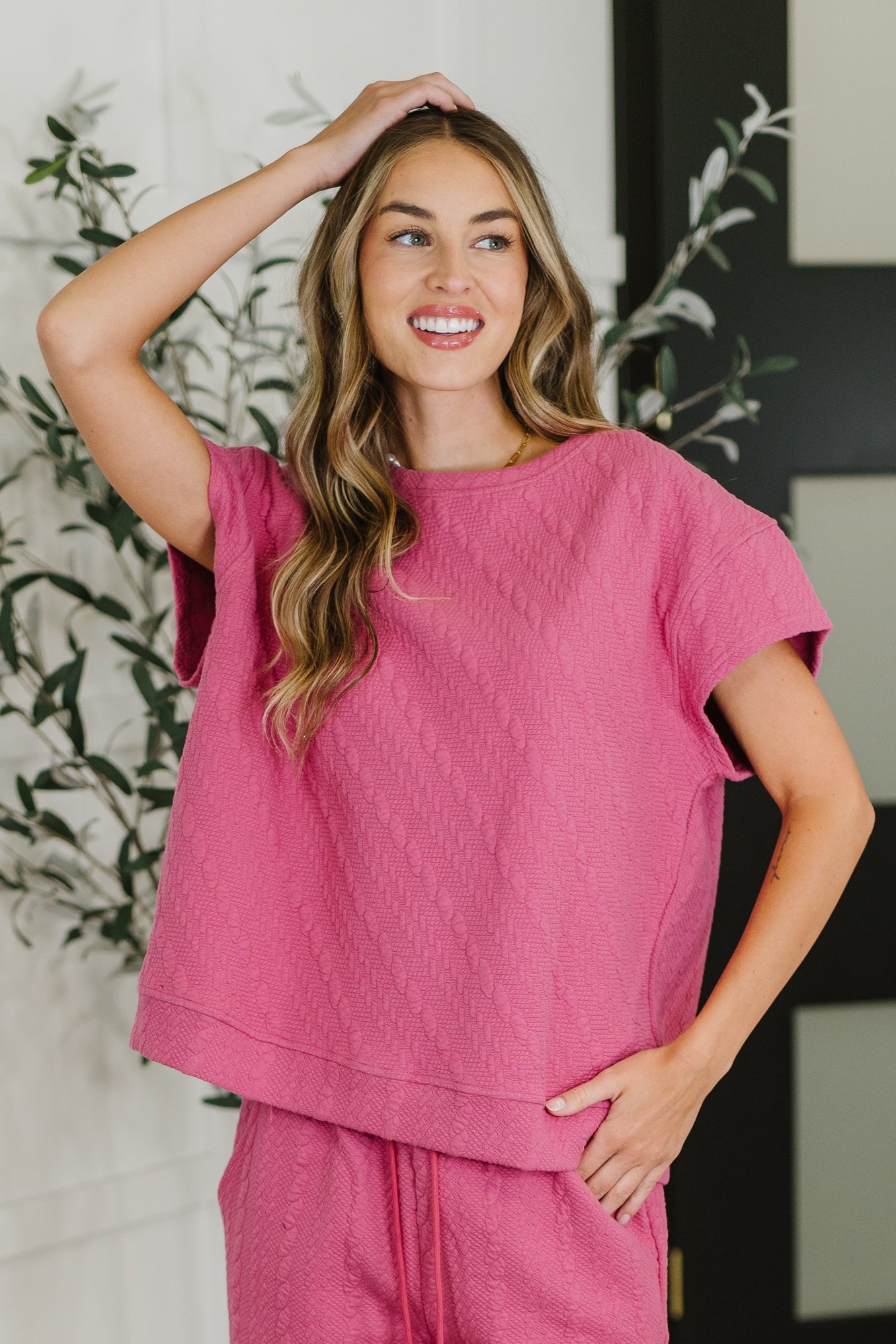 Woman wearing a pink outfit standing in a room with plants.