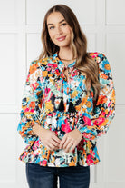 Woman wearing a colorful floral blouse against a white tiled wall.