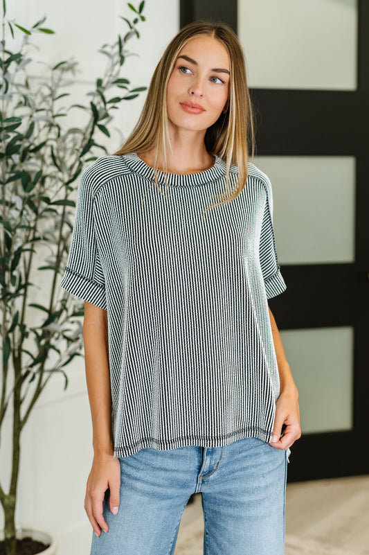 Woman wearing a striped shirt and jeans standing indoors with a plant in the background