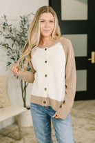 A woman wearing a beige button-down cardigan with raglan sleeves and a round neckline.