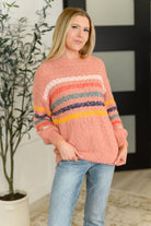 Woman wearing a pink sweater with colorful stripes indoors.