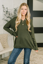 A woman wearing a dark olive Henley casual top with a v-neck and button closures.