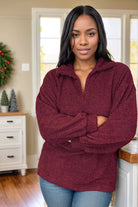 A woman wearing a burgundy sherpa sweater with a v-neck and long sleeves, standing indoors.