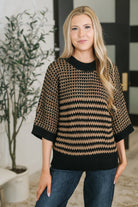 A woman wearing a black and tan knit sweater with a banded ribbed round neckline and dolman sleeves.