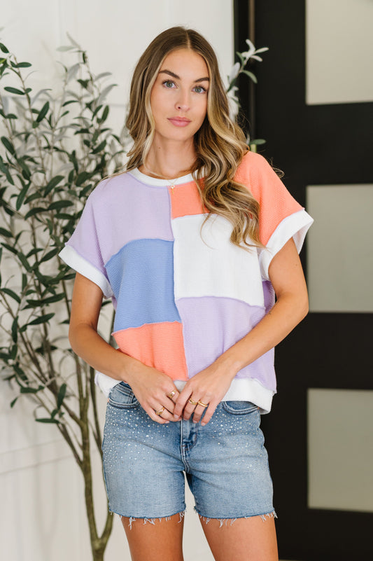 Woman wearing a colorful block-patterned shirt and denim shorts indoors.