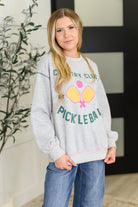 Woman wearing a gray sweatshirt with 'Pickleball' design in a casual setting