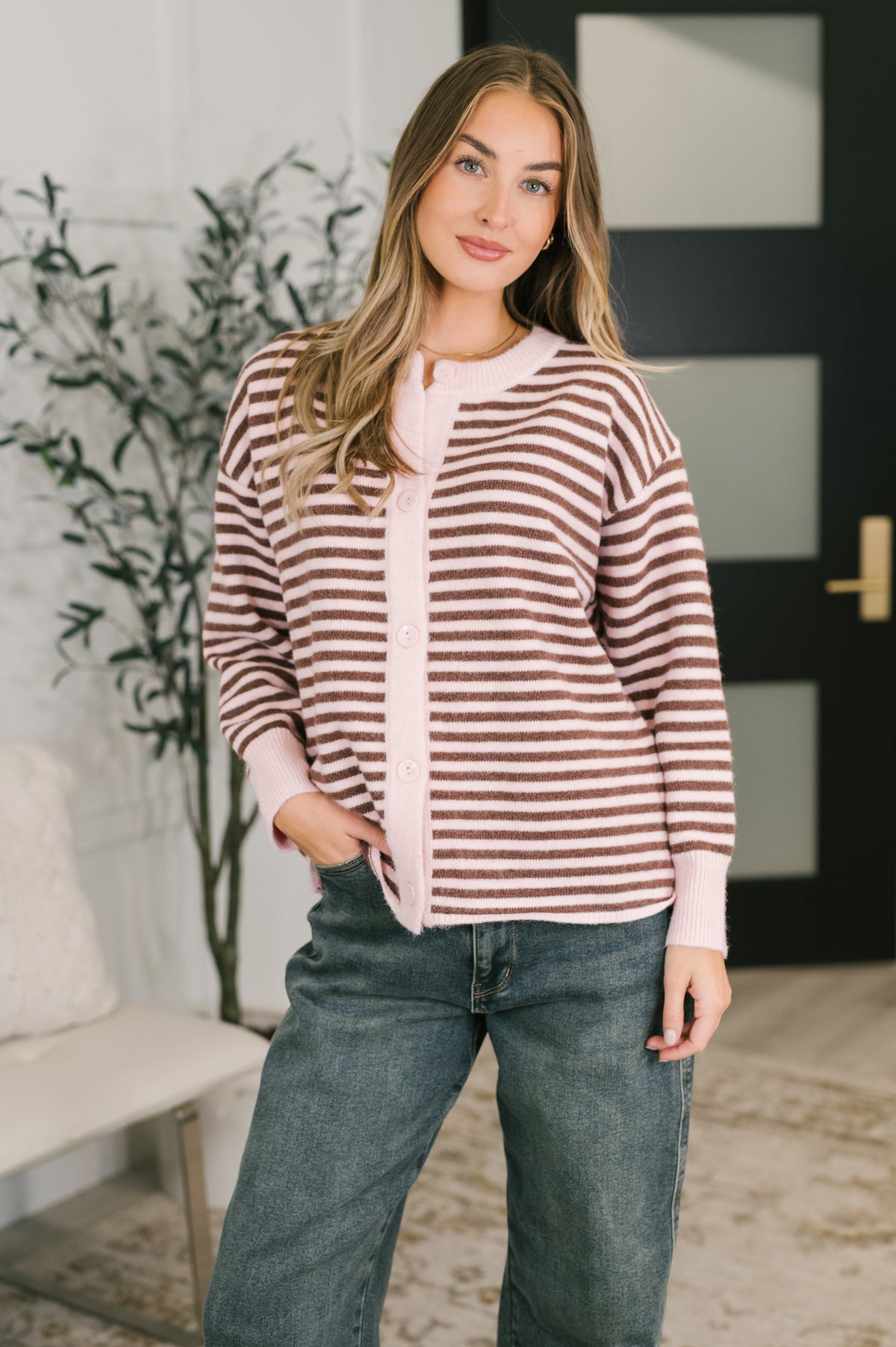 A woman wearing a pink and brown striped button-down cardigan with ribbed neckline and cuffs.