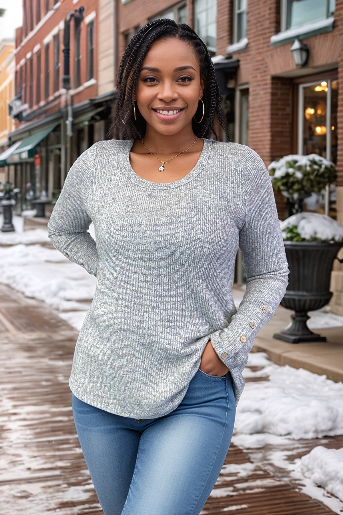 Grey pullover with a mini waffle knit, round neckline, and long sleeves featuring button cuffs.