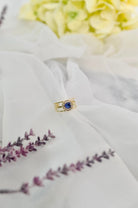 Gold tone open band ring with a blue cubic zircon stone on a soft white fabric surface.