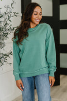 Woman wearing a green sweatshirt and blue jeans standing indoors.