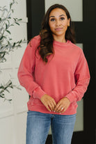 Woman wearing a pink sweatshirt and blue jeans standing indoors with a blurred background
