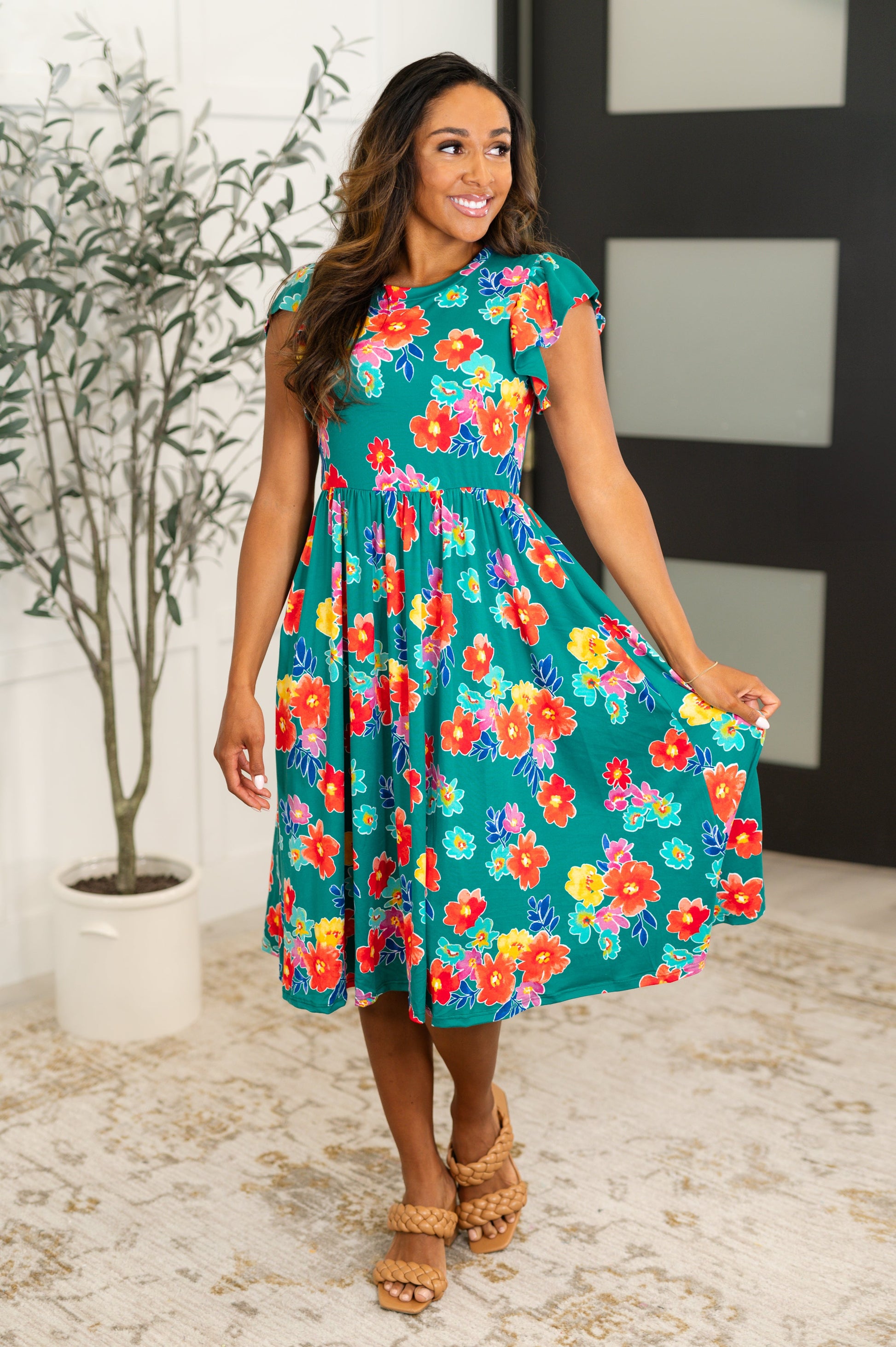 A woman wearing a green dress with a floral pattern, featuring a round neckline and flutter sleeves.