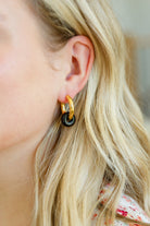 Close-up of a woman's ear wearing gold huggie earrings with a black stone bead.