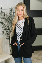 A model wearing a black button-down jacket with a collared V-neck and functional pockets.