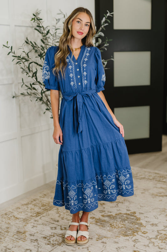 Woman wearing a blue dress with white embroidery indoors.