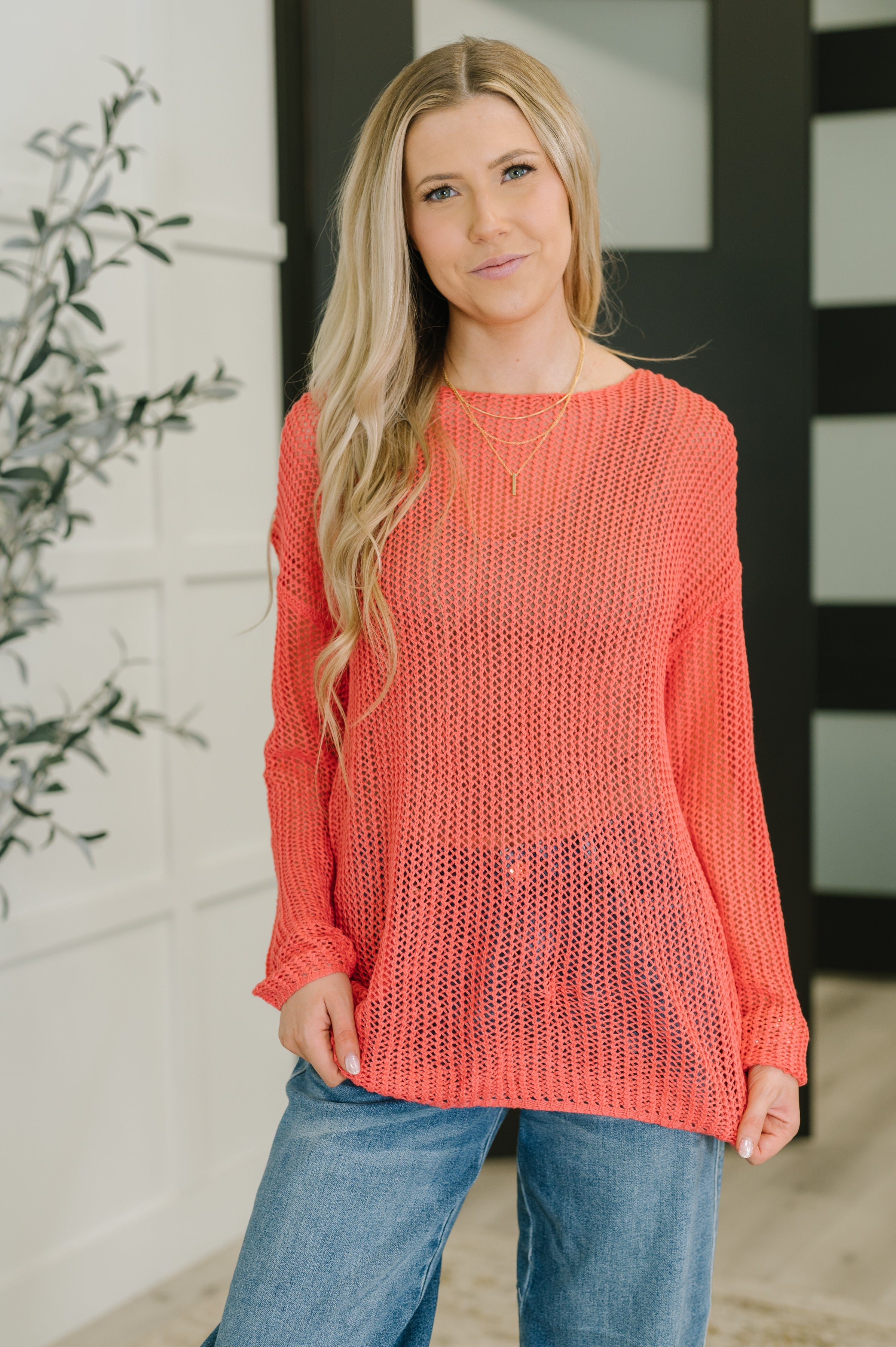 A woman wearing a coral loose knit sweater with a boat neckline and long sleeves.