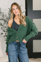A green cardigan with a v-neckline, bishop sleeves, and ribbed hem and cuffs, worn by a model in jeans.