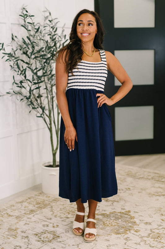 Woman wearing a striped and navy dress standing indoors with a plant and wall decor in the background.