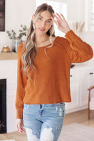 Woman wearing a orange rust-colored sweater and blue jeans in a home setting