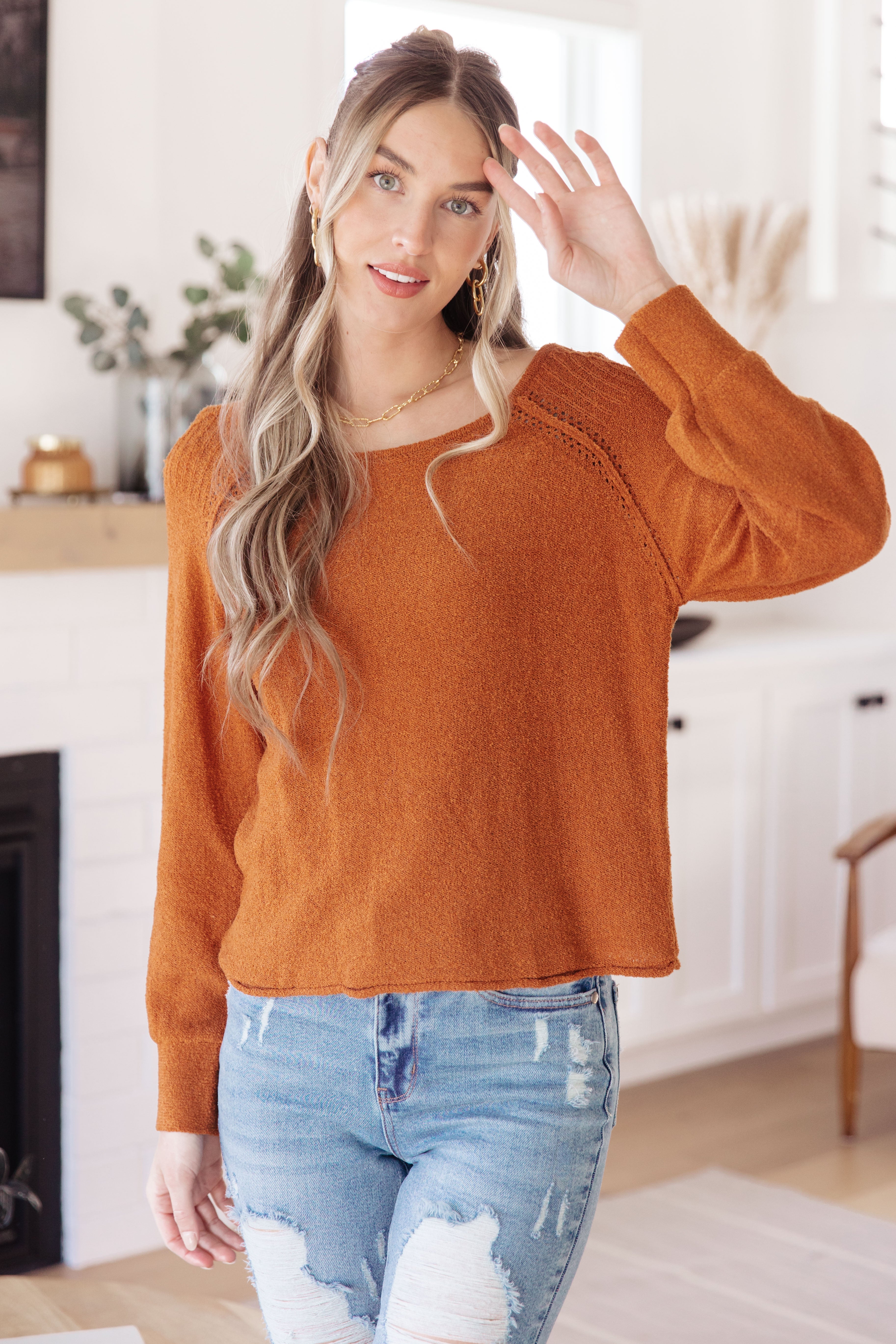 Woman wearing a orange rust-colored sweater and blue jeans in a home setting