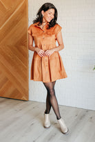Woman wearing an orange dress standing against a white brick wall.