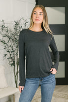 A woman wearing a charcoal long sleeve top with a banded round neckline.