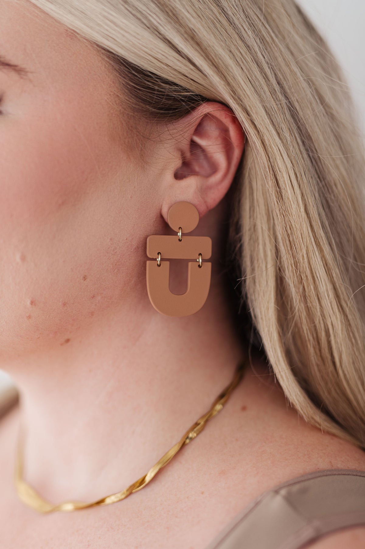 Brown earrings with a round top and geometric drop design, worn by a person.