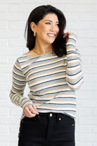 Woman wearing a striped long-sleeve top against a white brick wall.