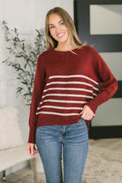 A woman wearing a burgundy relaxed sweater top with white horizontal stripes and jeans.