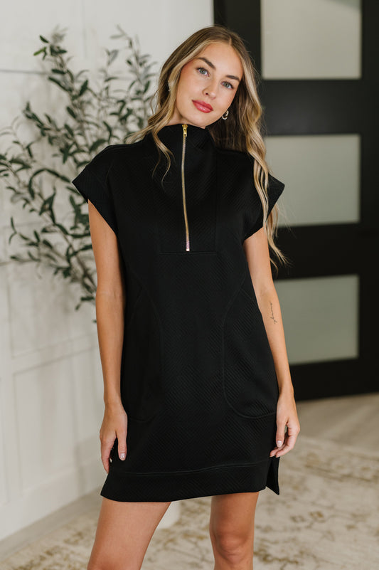 Woman wearing a black dress with a gold zipper in a room with decorative elements.