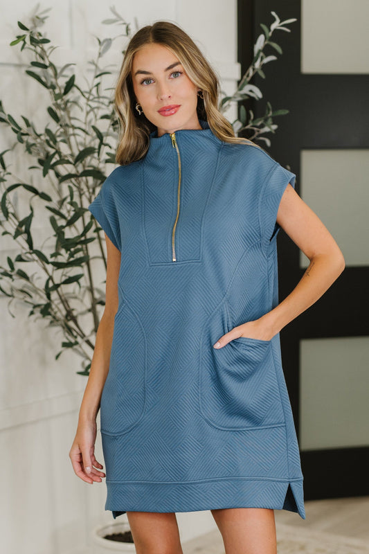 Woman wearing a blue dress with a zipper in a room with plants.