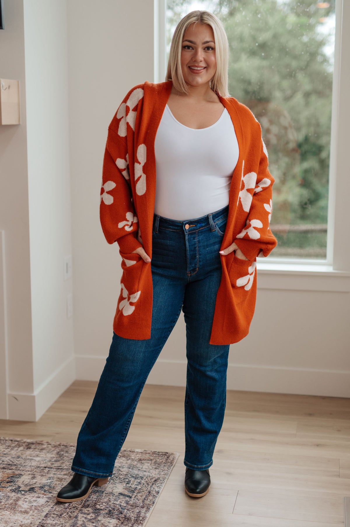 A woman wearing an oversized burnt orange cardigan with large floral patterns, open front, and balloon sleeves.