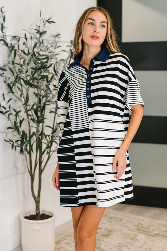 Woman wearing a black, white and navy striped dress standing indoors with a plant in the background