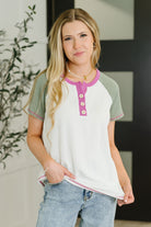 Woman wearing a white and green short-sleeve shirt with pink accents, standing indoors.